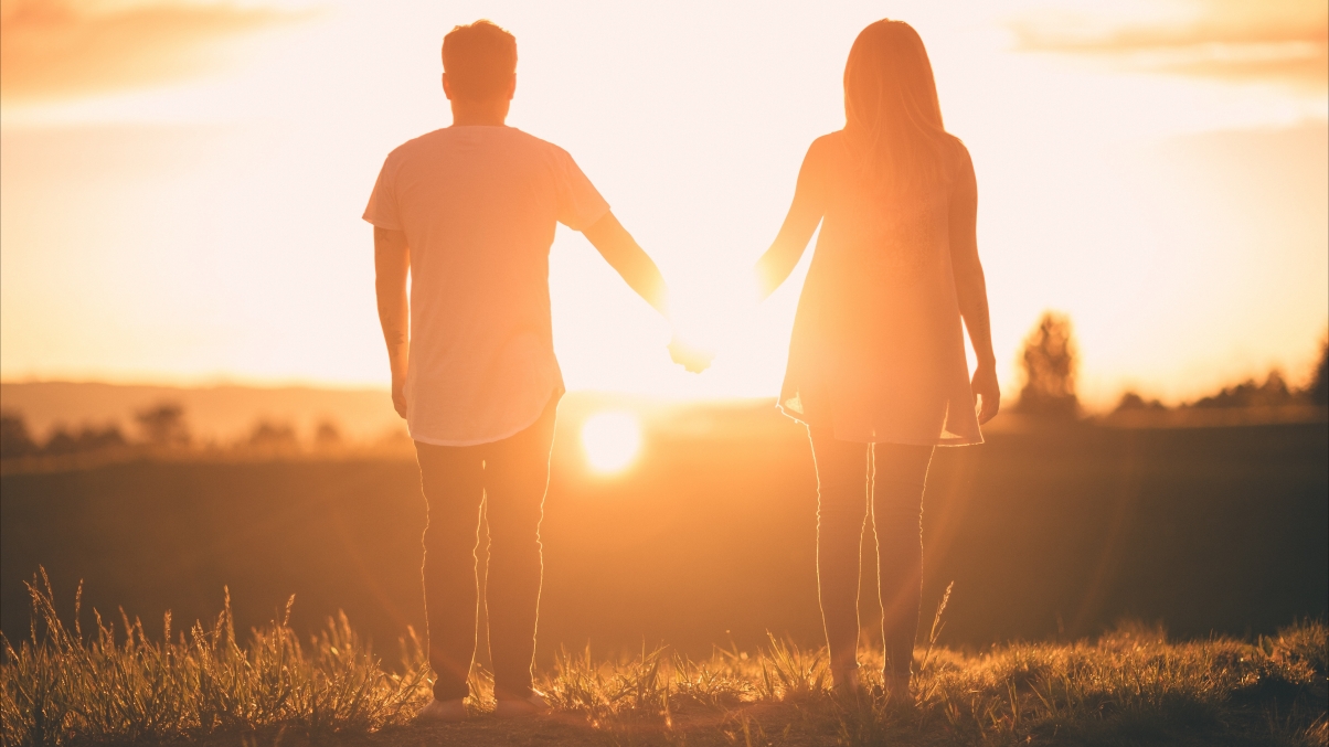 Woman and man hold hands at sunset