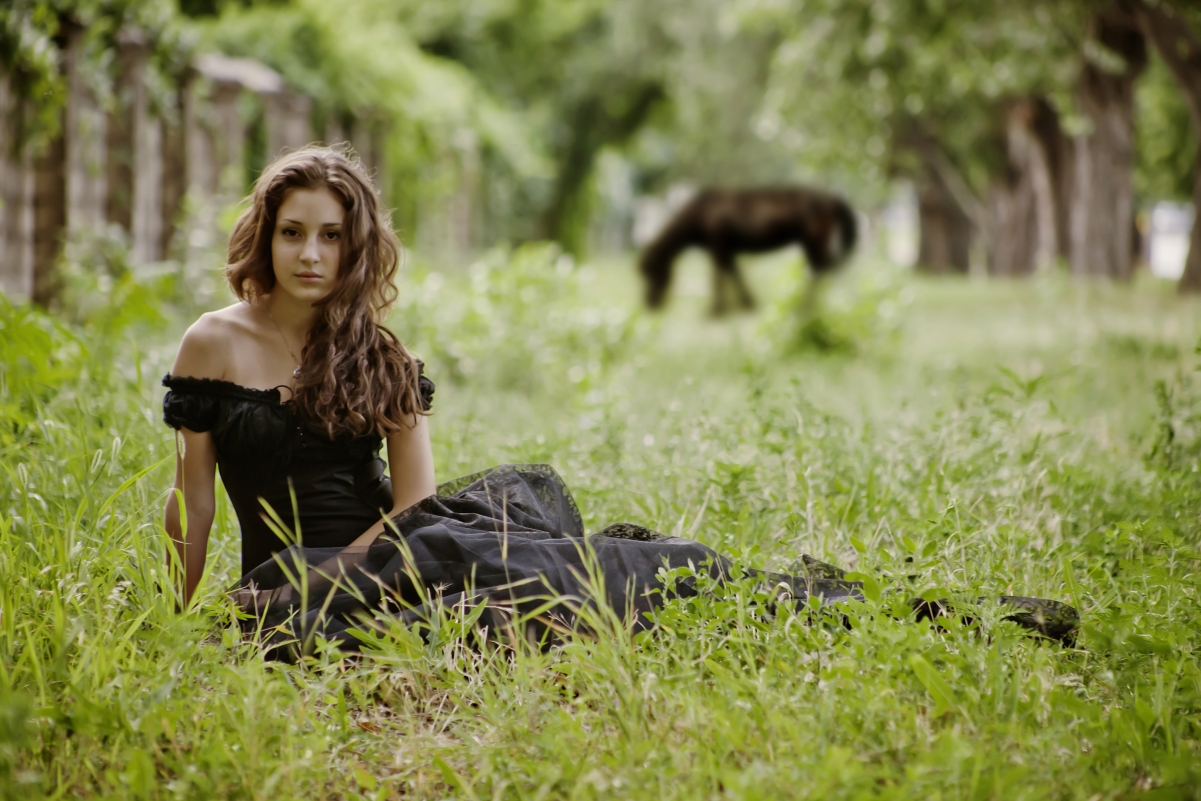 Beautiful woman in black dress sitting on the grass