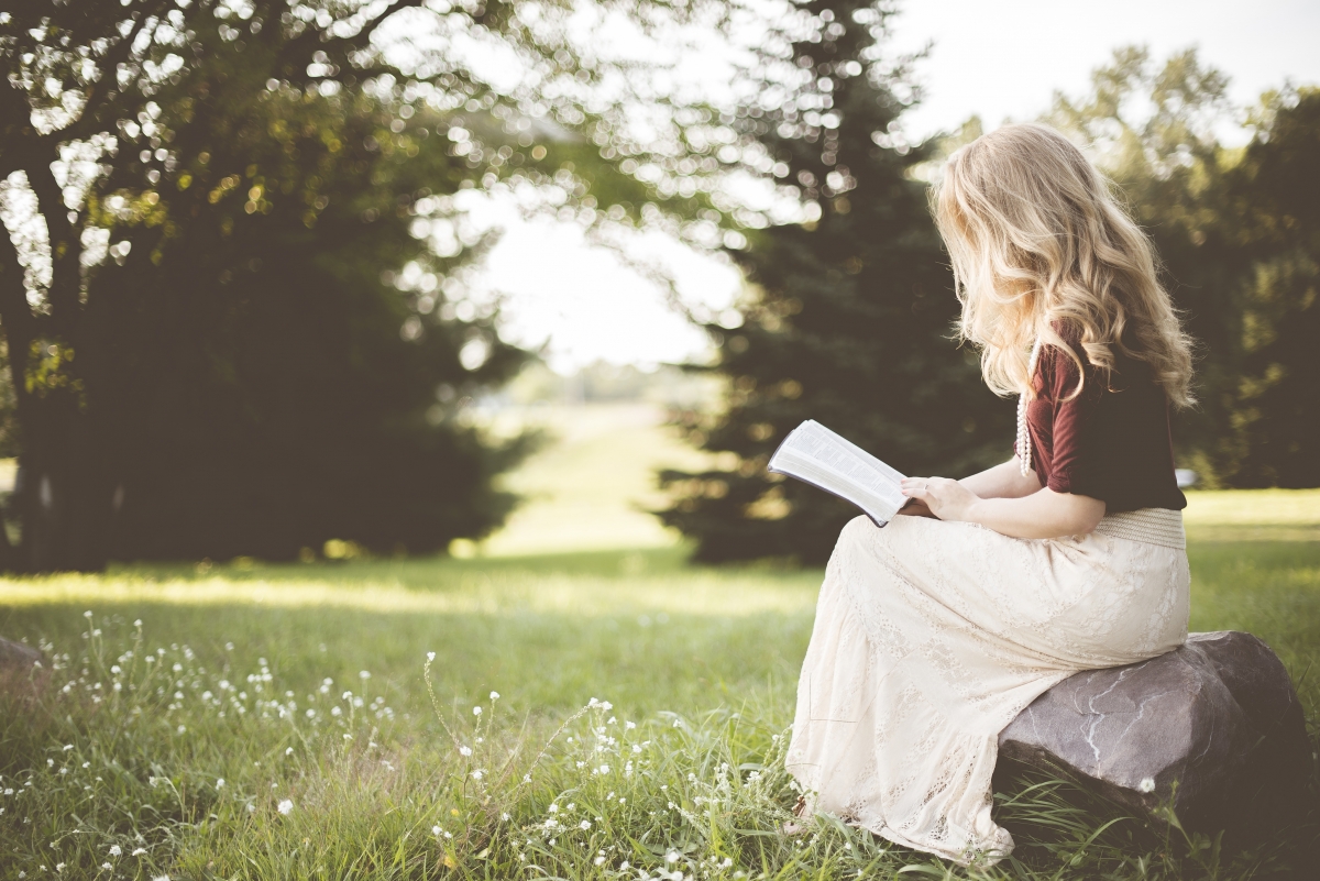 Blonde woman reading on grass outdoors