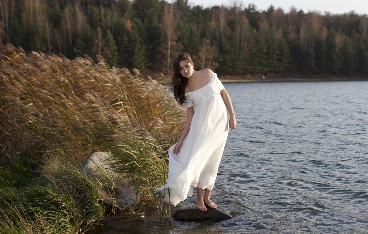 Beautiful brown-haired woman in a white skirt by the river