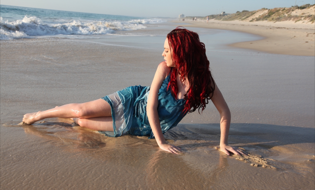Girl with red hair poses on the beach