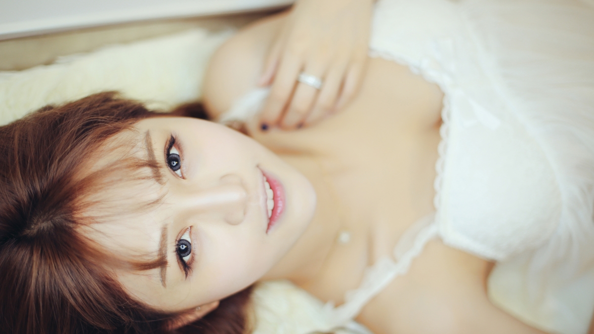 Cute beautiful woman in white pajamas writing on bed